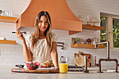 Portrait of smiling woman enjoying healthy breakfast in kitchen\n