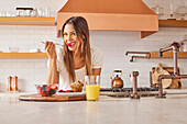 Portrait of smiling woman enjoying healthy breakfast in kitchen\n