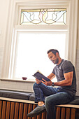 Mann liest ein Buch und sitzt zu Hause am Fenster
