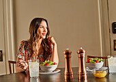 Lächelnde Frau genießt Salat am Tisch zu Hause
