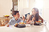 Lächelnder Junge (8-9) und Mädchen (12-13) beim Frühstück in der Küche