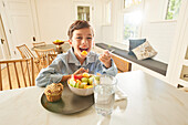 Smiling boy (8-9) enjoying breakfast in kitchen\n