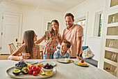 Smiling family with two children (8-9, 12-13) eating fresh fruit in kitchen\n