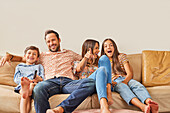 Smiling family with two children (8-9, 12-13) watching TV on sofa\n