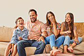 Lächelnde Familie mit zwei Kindern (8-9, 12-13) auf dem Sofa sitzend