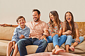 Portrait of smiling family with two children (8-9, 12-13) sitting on sofa\n