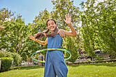Lächelndes Mädchen (12-13) spielt mit Hula-Hoop-Reifen im Park