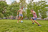 Father and son (8-9) playing soccer in park\n