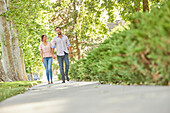Smiling couple holding hands, walking on treelined sidewalk\n
