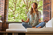 Mid adult woman meditating on sofa on patio\n