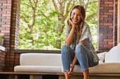 Portrait of smiling mid adult woman relaxing on sofa on patio\n