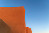 USA, New Mexico, Santa Fe, Moon in blue sky above adobe walls\n