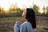 Side view of woman listening to music in meadow at sunset\n