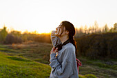 Portrait einer jungen Frau mit Kopfhörern auf einer Wiese bei Sonnenuntergang