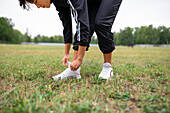 Young woman tying shoelaces while standing on grass\n