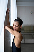 Ballerina leaning on wall with arms raised \n