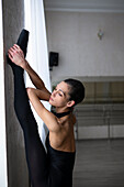 Ballet dancer stretching leg up on wall at dance studio \n
