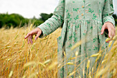 Young woman touching ears of wheat in field \n