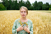 Portrait of young woman holding small wreath in wheat field \n