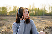 Young woman wearing headphones and sitting in meadow \n