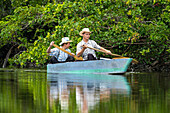 Two young Mennonite men fishing from a small homemade boat on the New River in the Orange Walk District of Belize.\n