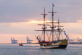 Frankreich, Calvados, Honfleur, Armada 2019, Grande Parade, Fregatte Etoile du Roy, die in der untergehenden Sonne die Seine-Mündung verlässt, mit dem Hafen von Le Havre im Hintergrund