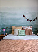 Double bed with patterned pillows in front of painted wall with ocean motif