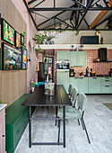 Open-plan kitchen with green cupboards, black dining table and artwork on the wall