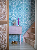 Pink console and staircase, blue patterned wallpaper in the hallway