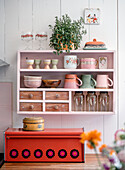 Shelf with crockery and potted plant above red bread box in the kitchen