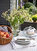 Gedeckter Gartentisch mit Apfelkorb, Gugelhupf und Gänseblümchenstrauß