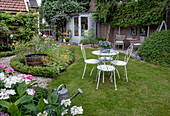 Ornamental garden with white metal revolving table and matching chairs in summer