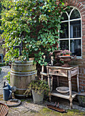 Rustikaler Gartentisch mit Blumenkübel und alter Weinfasspumpe vor Backsteinfassade