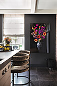 Modern kitchen with bar stools, dark wall colour and flower painting on the wall