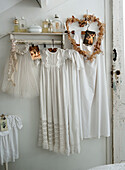 White clothes with romantic, feminine details on the wall shelf, old Christmas cards and heart-shaped wreath with dried flowers