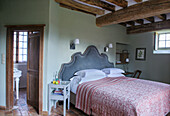 Double bed with high, upholstered headboard in rustic bedroom with ceiling beams