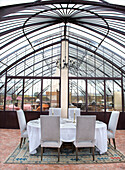 Festlich gedeckter Tisch in elegantem Wintergarten mit Glasdach und Kronleuchter