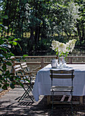 Table with white tablecloth and flowers and vintage garden chairs on a sunny terrace