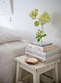 White bedside table in shabby chic style with stack of books and hydrangea in glass vase