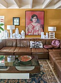 Corner sofa in brown leather in living room with yellow wall and art objects