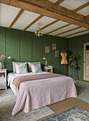 Bedroom with green wall paneling, wooden beamed ceiling and striped bedspread