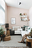 Living room with white corner sofa, wall shelves and pink wall paint