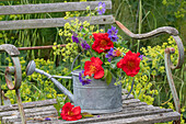 Blumenstrauss aus Storchschnabel (Geranium) und Purpurblütiges Leinkraut (Linaria purpurea) und rote Strauchrosen 'So Pretty' (Rosa) in alter Gießkanne