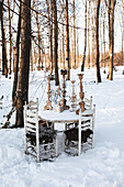 Weißer Gartentisch mit Kerzenständern im verschneiten Wald