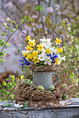 Daffodils (Narcissus) 'Sailboat', 'Tete a Tete', dwarf iris (Iris Reticulata) 'Harmony' in vase with Easter nest and Easter eggs