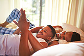 Young gay male couple holding hands on bed