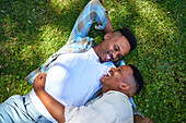 Affectionate gay male couple laying in grass