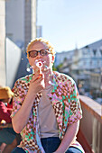 Young man blowing bubbles on sunny balcony