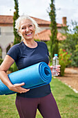 Senior woman with yoga mat in summer garden