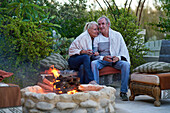Senior couple sitting and drinking wine at fire pit